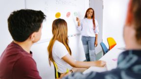 A female student showing and explaining something on a whiteboard in front of a class.