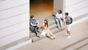 Four international students sitting and standing in the entrance area of a university building.