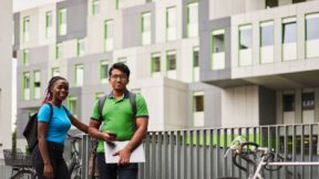 Two students are standing in the courtyard of a student dormitory.