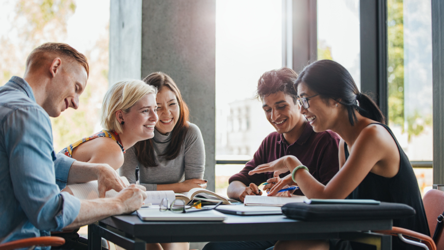 International students sit laughing at a table in the university and study together.